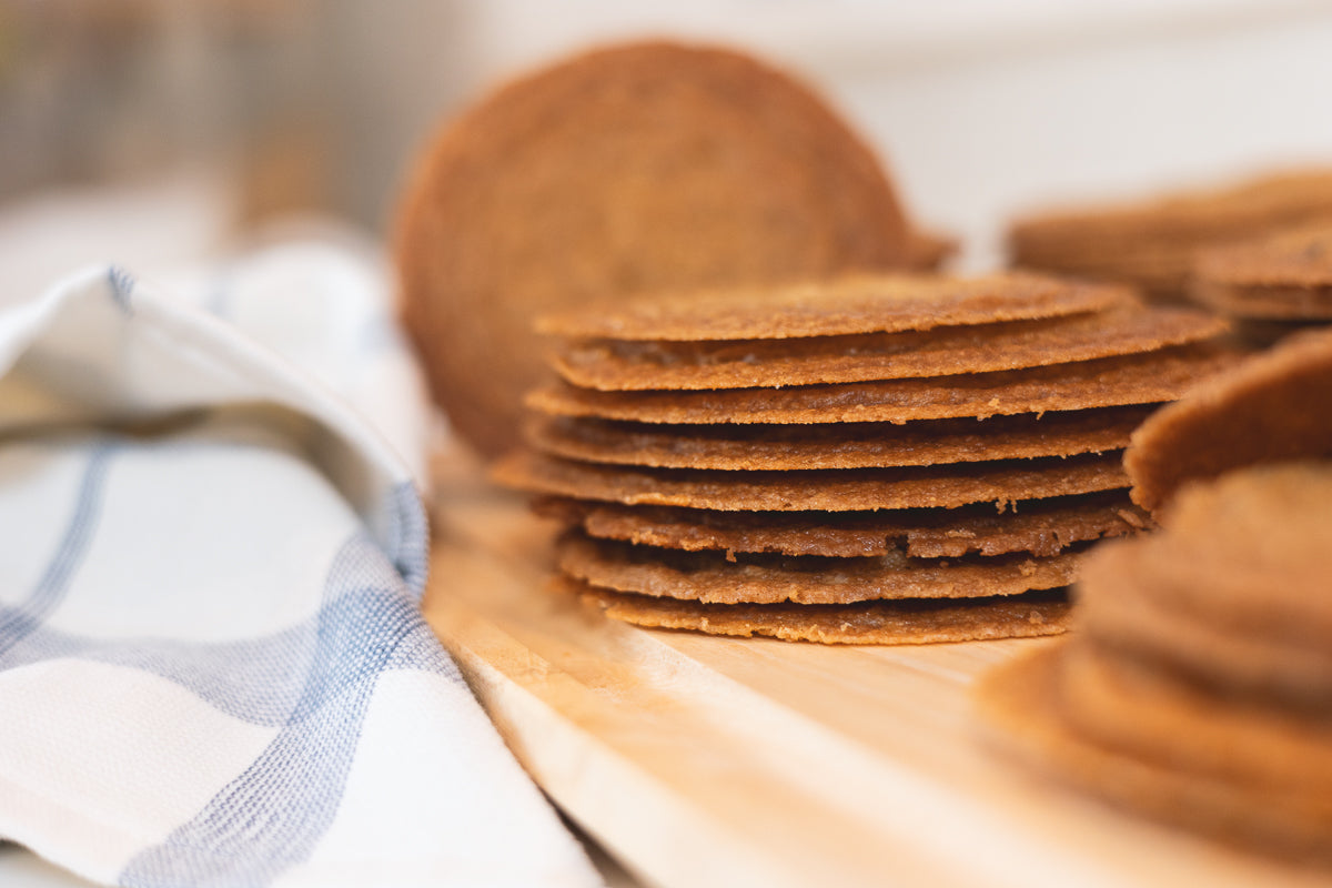 Stacks of golden brown chocolate chip cookies on a surface with a blue and white striped cloth in the background.